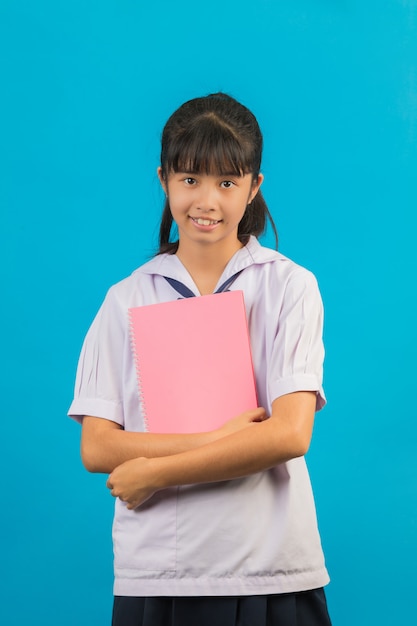 Photo gratuite Étudiant asiatique avec fille cheveux longs tenant un cahier sur un bleu.