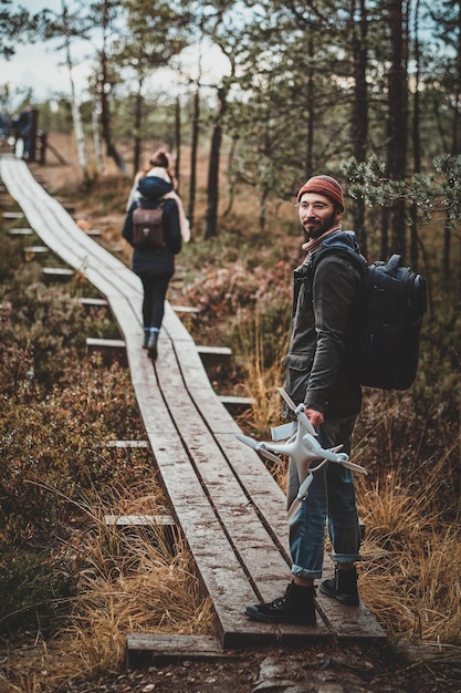 Un étudiant barbu à la mode profite d'une promenade d'automne avec son drone dans le parc.