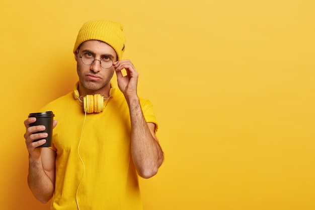 Un étudiant sérieux garde la main sur le bord des lunettes, a une expression fatiguée