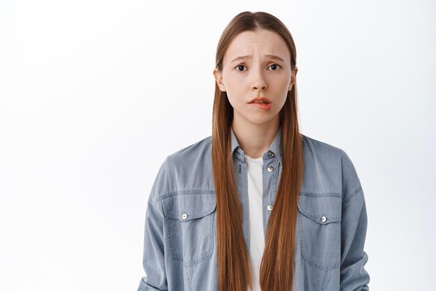 Une étudiante adolescente préoccupée et inquiète se mordant la lèvre et fronçant les sourcils à la sensation de nervosité effrayée ou anxieuse debout troublée sur fond blanc