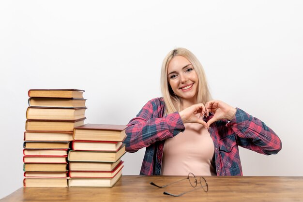 étudiante assise avec différents livres souriant sur blanc