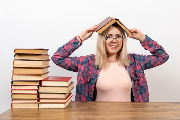 étudiante assise avec des livres en tenant un sur sa tête sur blanc