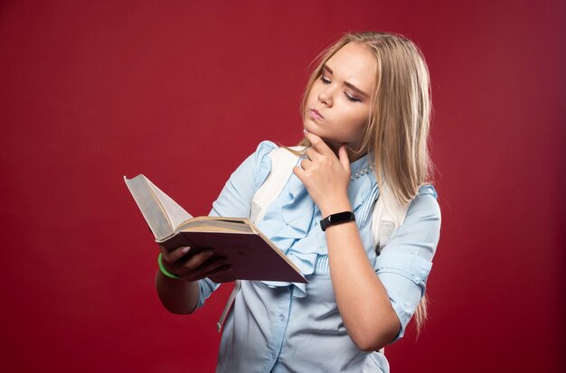 Une étudiante blonde lit un livre et réfléchit attentivement.