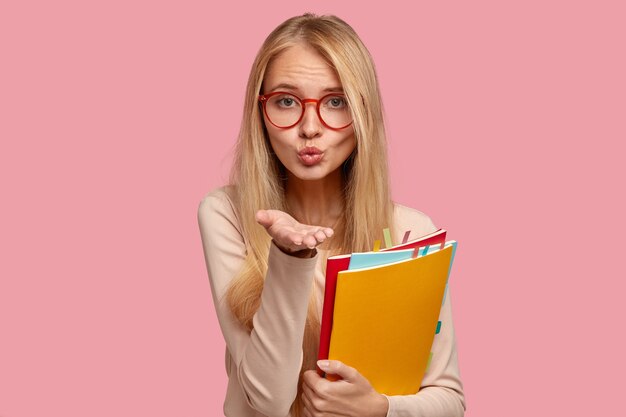 étudiante blonde posant contre le mur rose