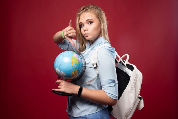 Une étudiante blonde tient un globe et pointe un endroit.