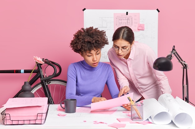 Une étudiante de la faculté d'architecture discute d'idées pour de futurs travaux de projet étudie attentivement la pose de document papier au bureau avec des plans et des autocollants autour du brainstrom sur une tâche importante