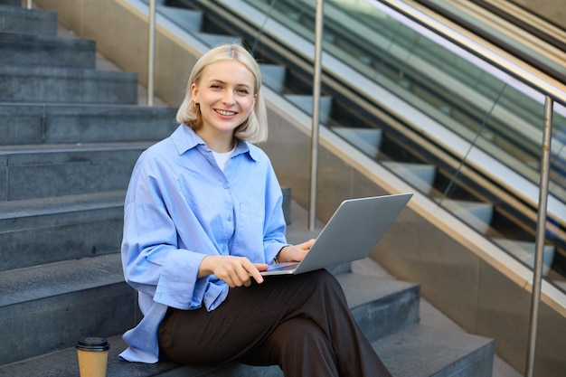 Photo gratuite une étudiante souriante utilisant un ordinateur portable, un appareil de technologie moderne en plein air sur le campus universitaire