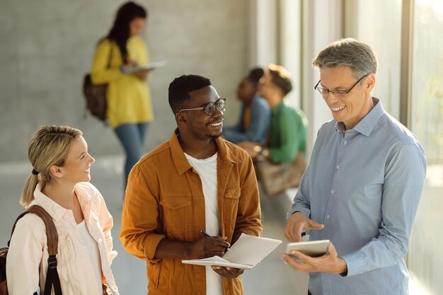 Des étudiants heureux et leur professeur utilisant un pavé tactile dans le couloir de l'université