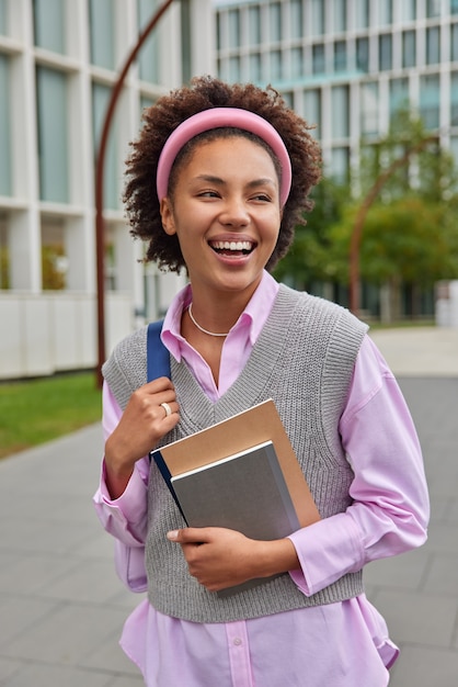 les étudiants se promènent dans la cour du collège porte un sac à dos et des blocs-notes, une chemise rose, un gilet et un cerceau en tricot entourés d'une rue de la ville expriment des émotions positives