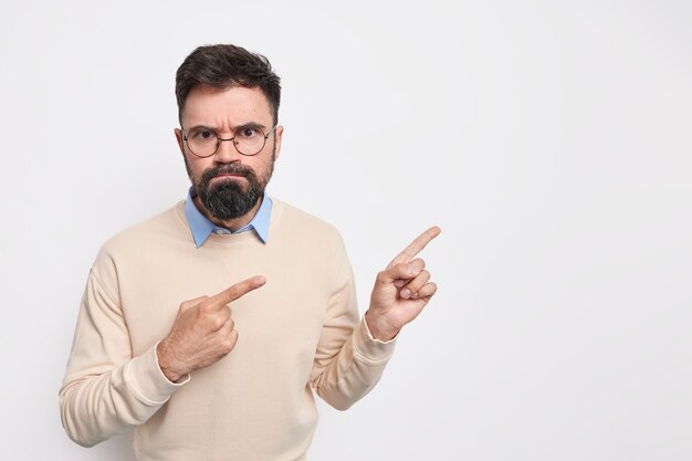 Un Européen barbu sérieux et mécontent avec une expression sceptique sent que le mécontentement gronde quelqu'un porte des lunettes rondes et un pull