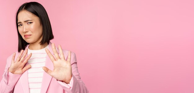 Evadez-vous Femme d'affaires asiatique dégoûtée rejetant la poignée de main pour refuser de grimacer de l'aversion décliner qch avec aversion posant en costume sur fond rose