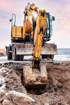 Une excavatrice puissante creuse une fosse de fondation pour la construction d'un immeuble résidentiel. chargement de la terre dans un camion à benne basculante. fabrication du bâtiment. les fouilles. fermer.