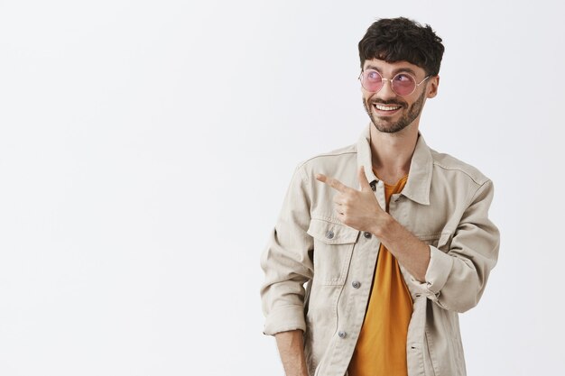 Excité beau mec posant contre le mur blanc avec des lunettes de soleil