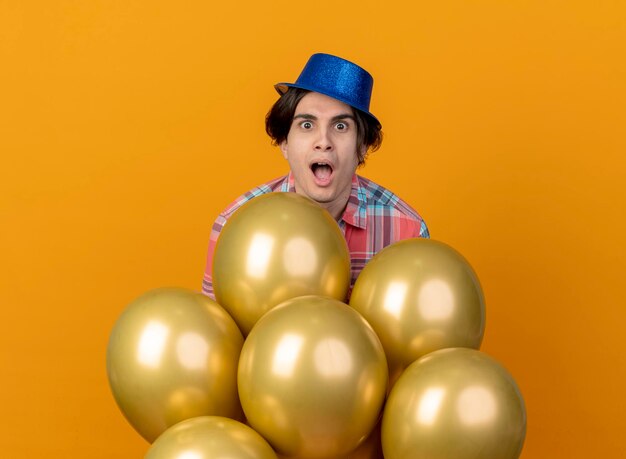 Excité bel homme caucasien portant chapeau de fête bleu se dresse avec des ballons d'hélium