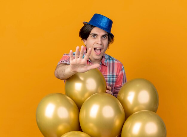 Excité bel homme caucasien portant chapeau de fête bleu se dresse avec des ballons d'hélium