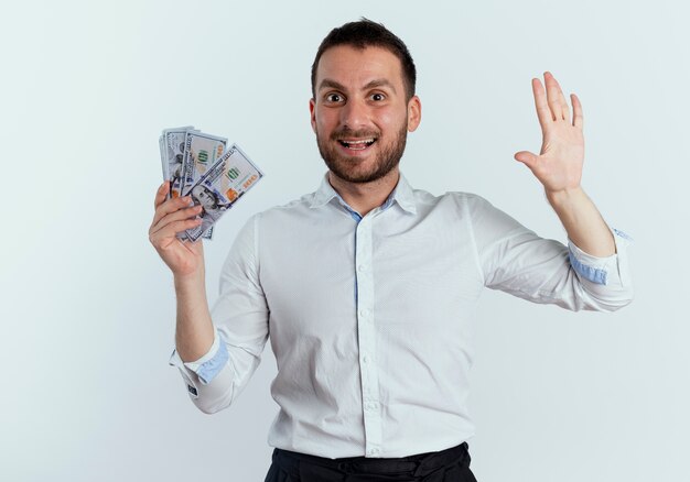 Excité bel homme détient de l'argent et soulève la main isolé sur un mur blanc