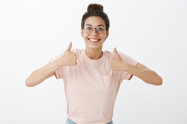 Photo gratuite excité belle fille avec des lunettes posant contre le mur blanc