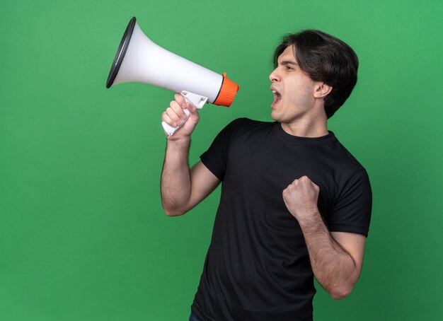 Excité à côté jeune beau mec portant un t-shirt noir parle sur haut-parleur et montrant oui geste isolé sur mur vert