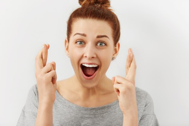 Excité et fasciné jeune femme de race blanche aux cheveux roux en gardant les doigts croisés pour la bonne chance