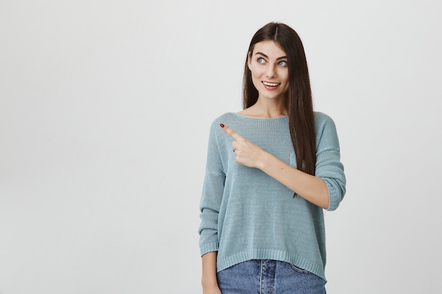 Excité femme intriguée souriant, doigt pointé vers la gauche