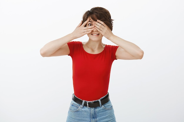 Excité femme souriante couvrir les yeux avec les mains, en attente de surprise, furtivement à travers les doigts étonné