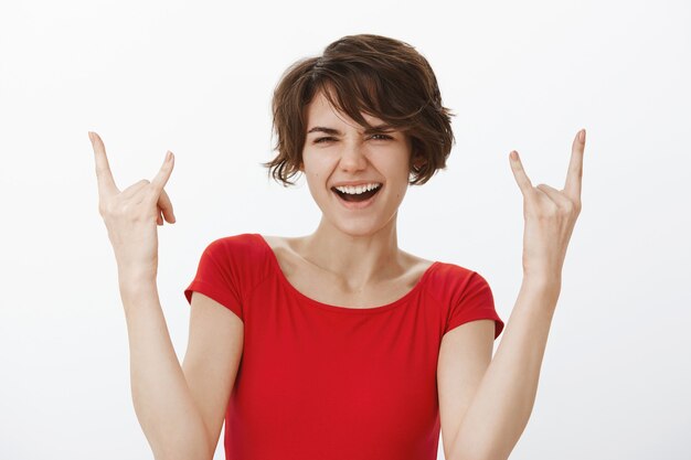 Excité femme souriante à la surprise et montrant le geste rock-n-roll, s'amusant