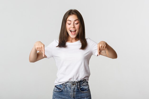 Excité fille brune heureuse, regardant et pointant vers le bas avec un sourire amusé.