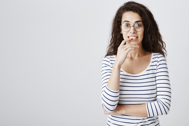 Excité fille curieuse dans des verres mordant le doigt et à la recherche intéressée