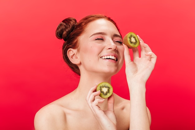 Excité fille européenne tenant kiwi. Photo de Studio de femme insouciante avec des fruits exotiques isolés sur fond rouge.