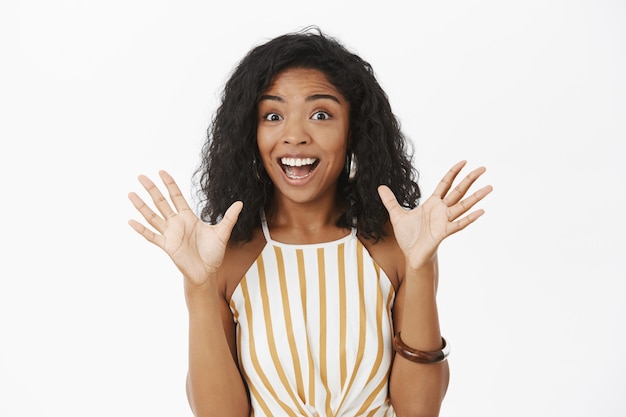 Photo gratuite excité heureux et expressif jolie femme afro-américaine avec une coiffure frisée soulevant des paumes