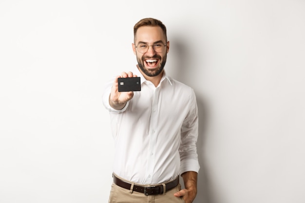 Excité homme caucasien dans des verres montrant la carte de crédit, concept de shopping.