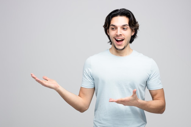 Excité jeune bel homme regardant à côté montrant les mains vides isolé sur fond blanc