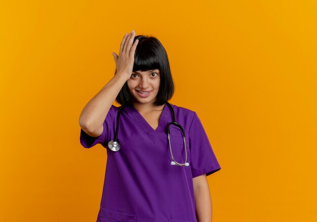 Excité jeune femme médecin brune en uniforme avec stéthoscope met la main sur la tête