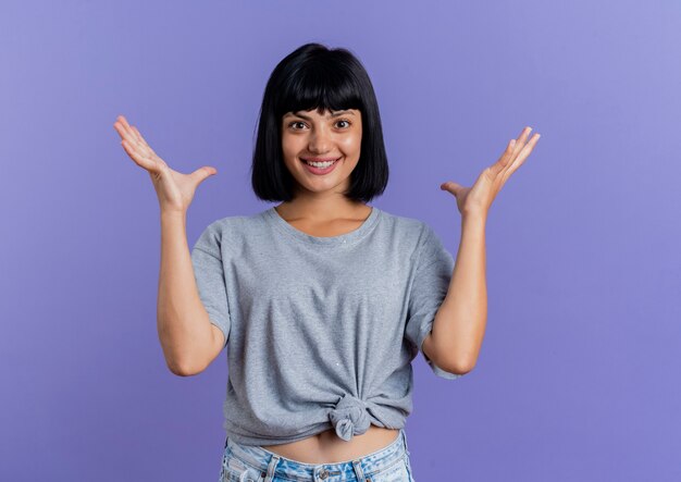 Excité jeune femme de race blanche brune se tient avec les mains levées en regardant la caméra isolée sur fond violet avec copie espace