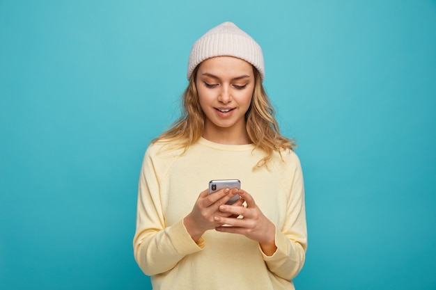 Excité jeune fille portant un chapeau d'hiver à l'aide de son téléphone portable