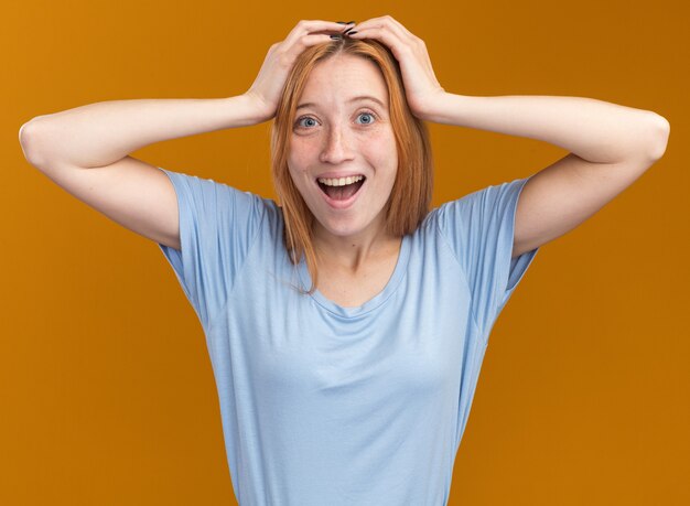 Excité jeune fille rousse au gingembre avec des taches de rousseur mettant les mains sur la tête orange