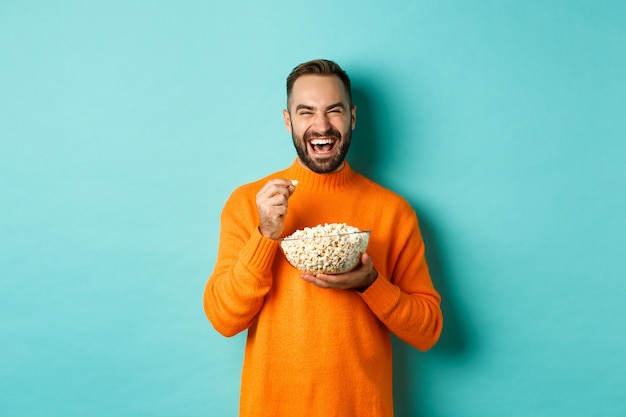 Excité jeune homme regardant un film intéressant sur l'écran de télévision, mangeant du pop-corn et à la stupéfaction