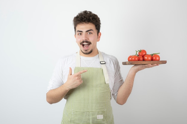 Excité jeune homme tenant un tas de tomates fraîches et pointant le doigt dessus.