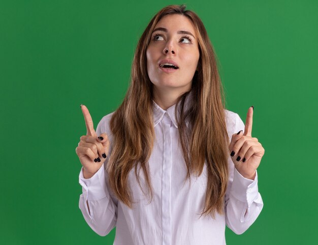 Excité jeune jolie fille caucasienne regarde et pointe avec deux mains sur le vert