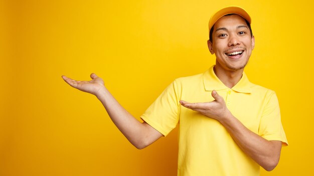 Excité jeune livreur portant casquette et uniforme pointant vers le côté avec les mains