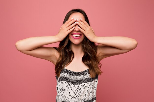 Excité jolie femme européenne avec une longue coiffure ondulée habillée robe lumineuse couvrant le visage avec les mains