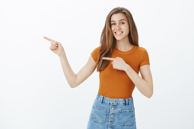 Excité jolie fille invitant à l'événement de départ, pointant du doigt la gauche et souriant, démontrant la bannière