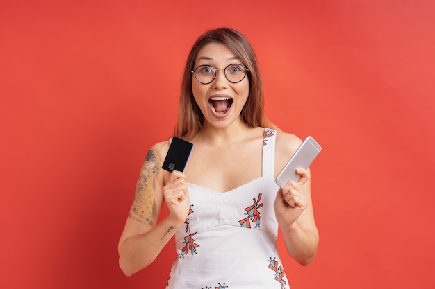 Excité de jolie jeune femme tenant le téléphone et la carte de crédit dans ses mains