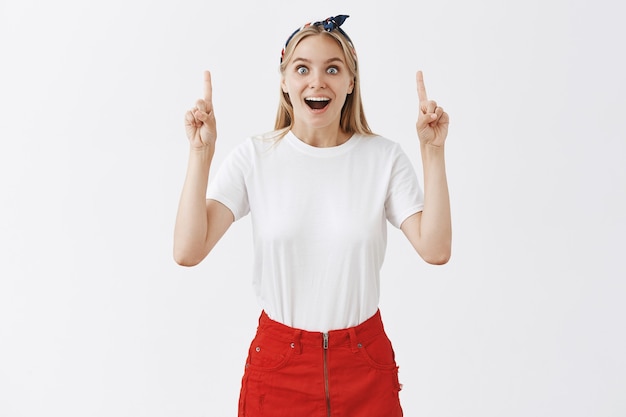 Excité joyeuse jeune fille blonde posant contre le mur blanc