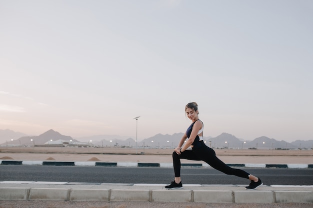 Excité joyeux incroyable femme heureuse qui s'étend sur la route du pays tropical. Souriant vers le bas, exprimant la positivité, les vraies émotions, le mode de vie sain, l'entraînement.