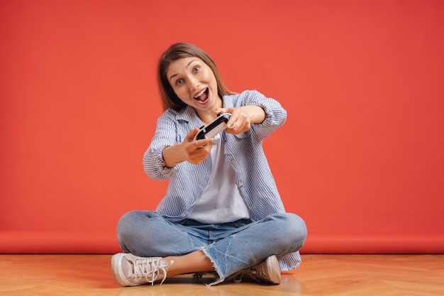 Excité occasionnel jeune femme jouant à des jeux vidéo s'amuser sur le mur rouge