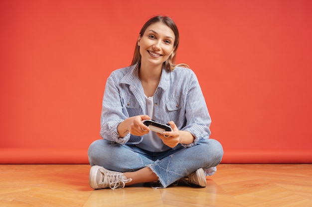 Excité occasionnel jeune femme jouant à des jeux vidéo s'amuser sur le mur rouge