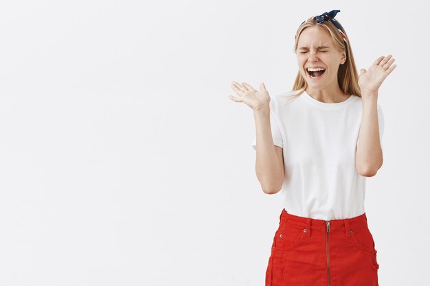 Excité et réjouissant jeune fille blonde posant contre le mur blanc