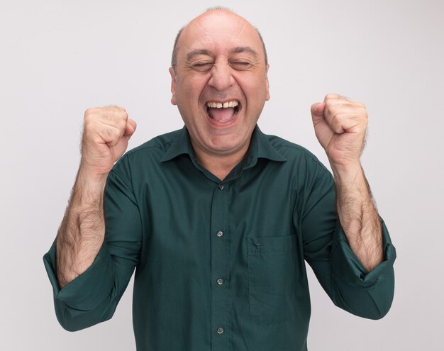 Excité avec les yeux fermés homme d'âge moyen portant un t-shirt vert montrant oui geste isolé sur mur blanc