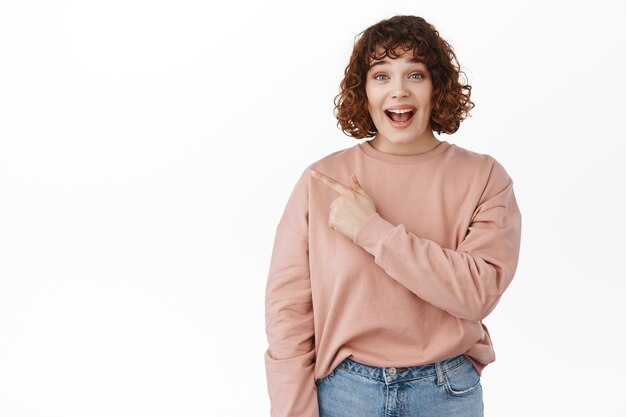 Excitée fille caucasienne haleter, dire wow et pointant vers le coin supérieur gauche avec un visage surpris et impressionné, vérifiant la publicité, des nouvelles étonnantes, debout sur fond blanc.